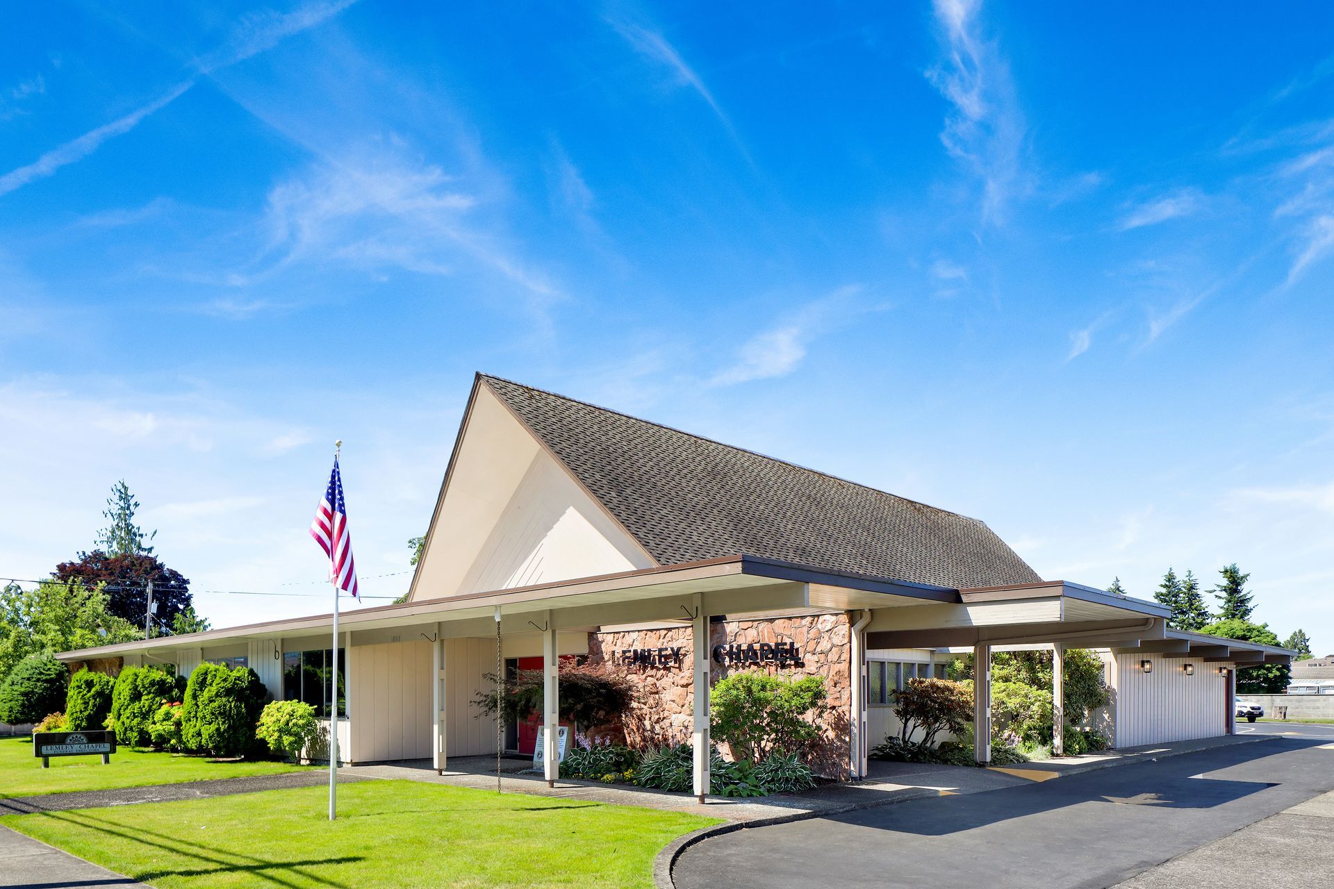 Low, tan building with a steep roof, covered entrance, and American flag under a bright blue sky