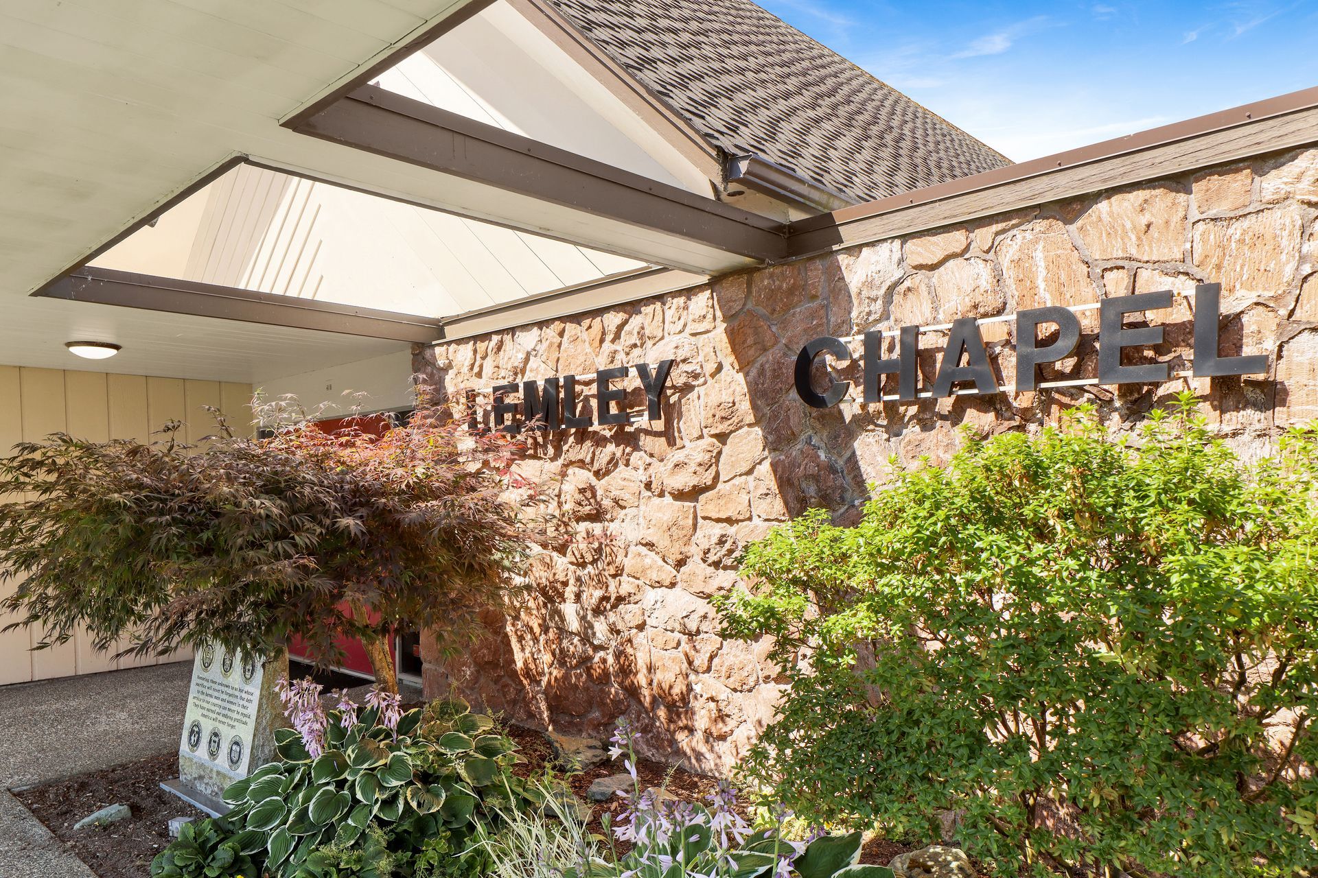 Entrance to a stone chapel with a covered awning and greenery in front