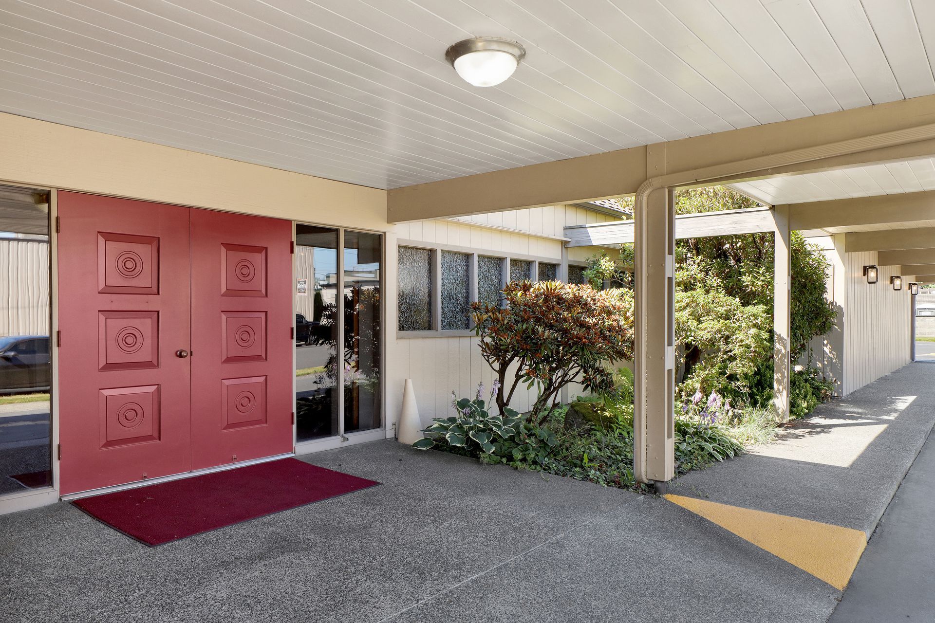 Entrance to a building with a red front door, covered walkway, and landscaped side path