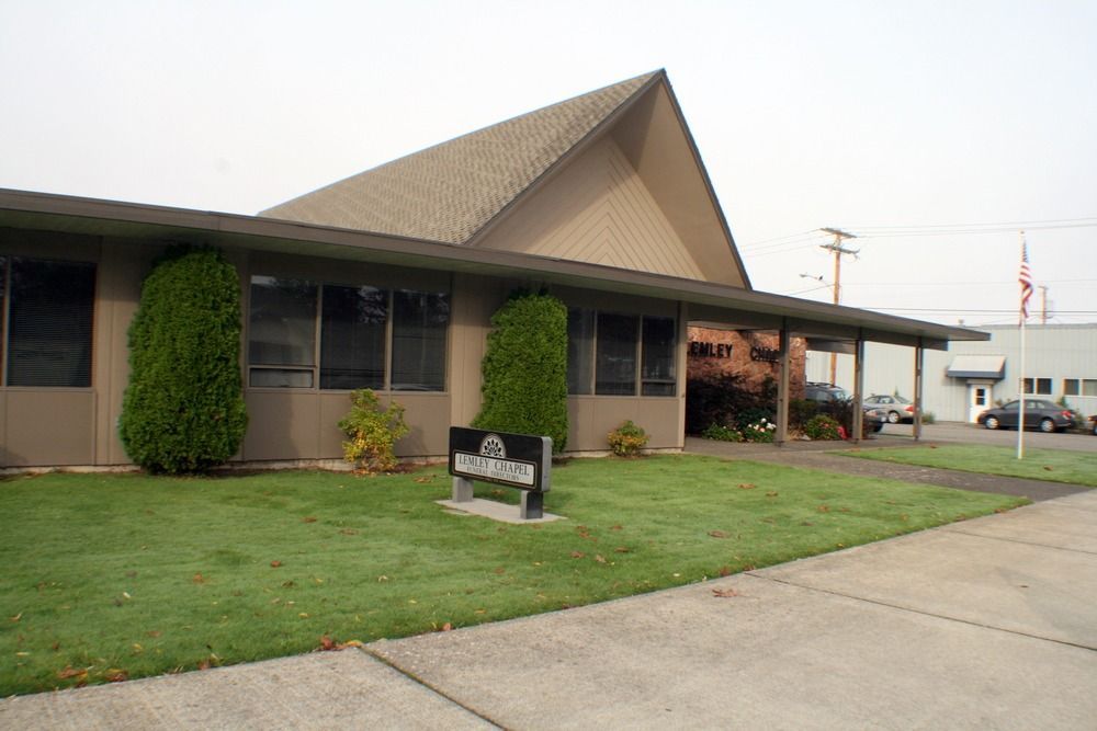Single-story building with brown roof, green lawn, and a sidewalk in front