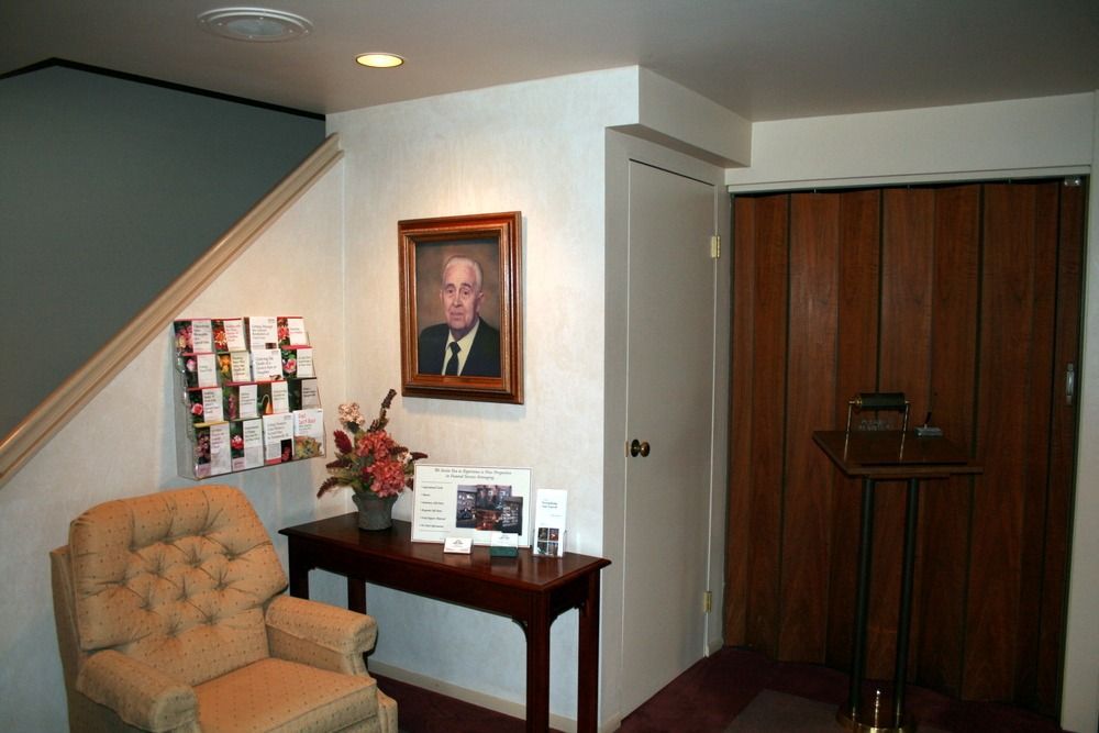 Small lobby with tan chair, side table, portrait, and wooden closet doors.