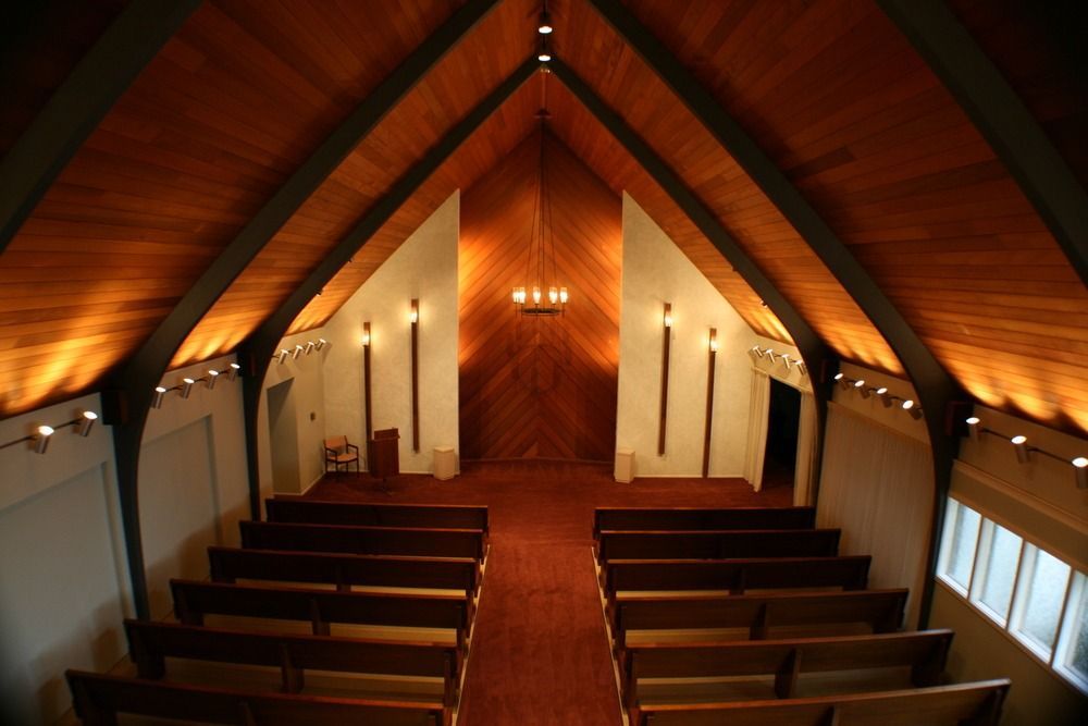Empty church sanctuary with wooden pews and vaulted wood ceiling, lit by warm wall sconces