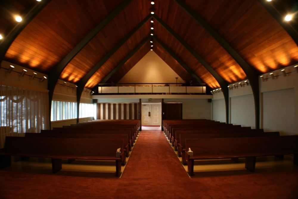 Empty wooden church interior with rows of pews and a red carpet aisle under a vaulted ceiling