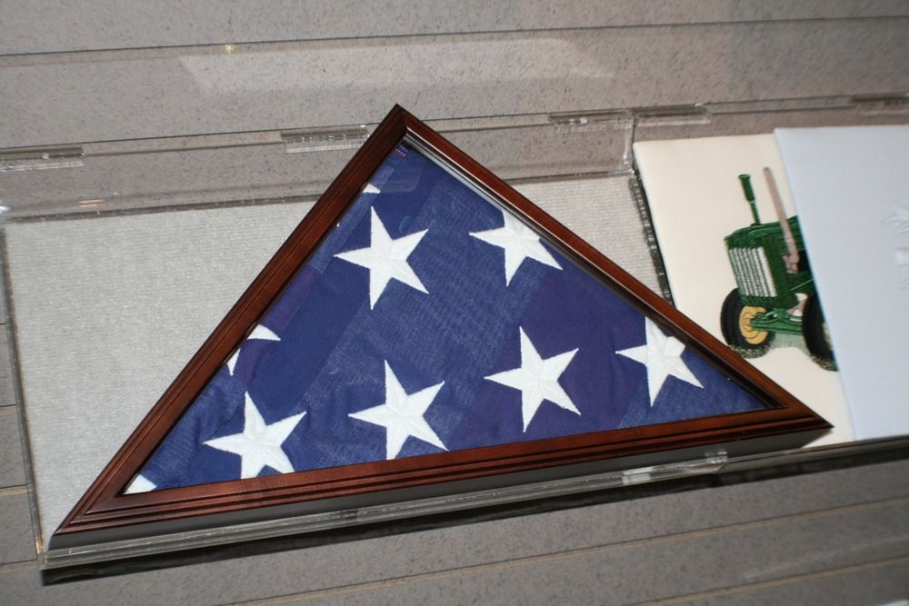 Folded U.S. flag with white stars in a wooden triangular display case on a shelf