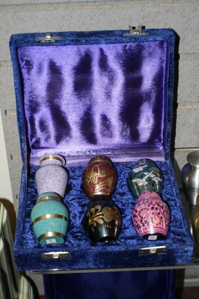 Open blue velvet box holding five small decorated glass bottles on purple satin lining