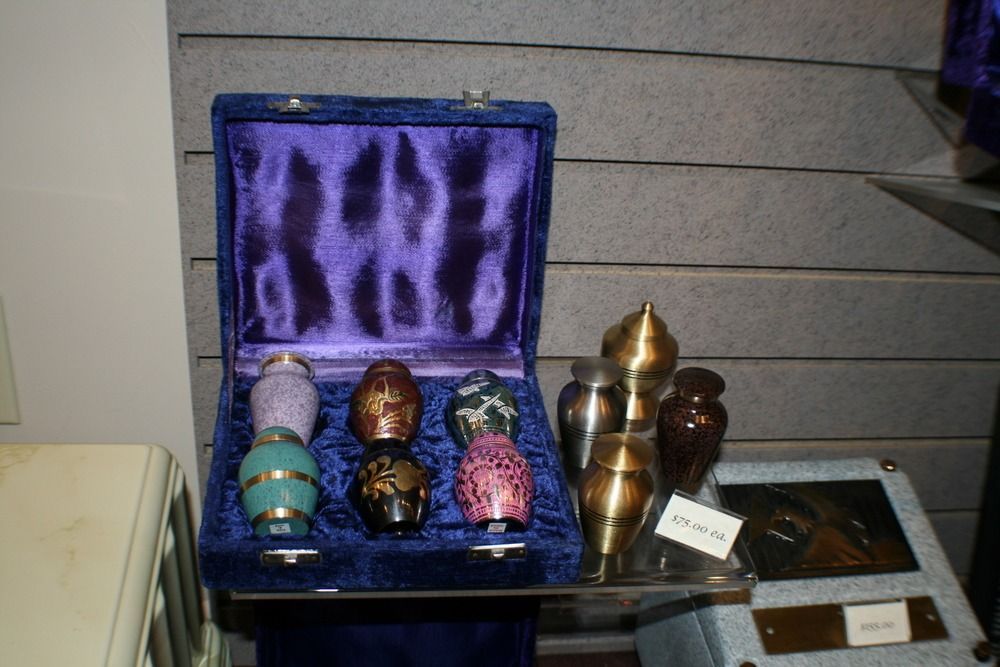 Display of decorative urns in a blue velvet case beside brass urns on a table