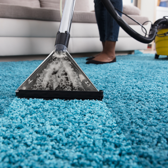 Person vacuuming a bright blue carpet in a living room; a yellow vacuum cleaner is in the background.