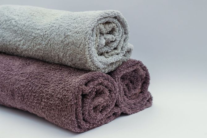 Three rolled towels, one gray, two dark purple, stacked on a white surface.