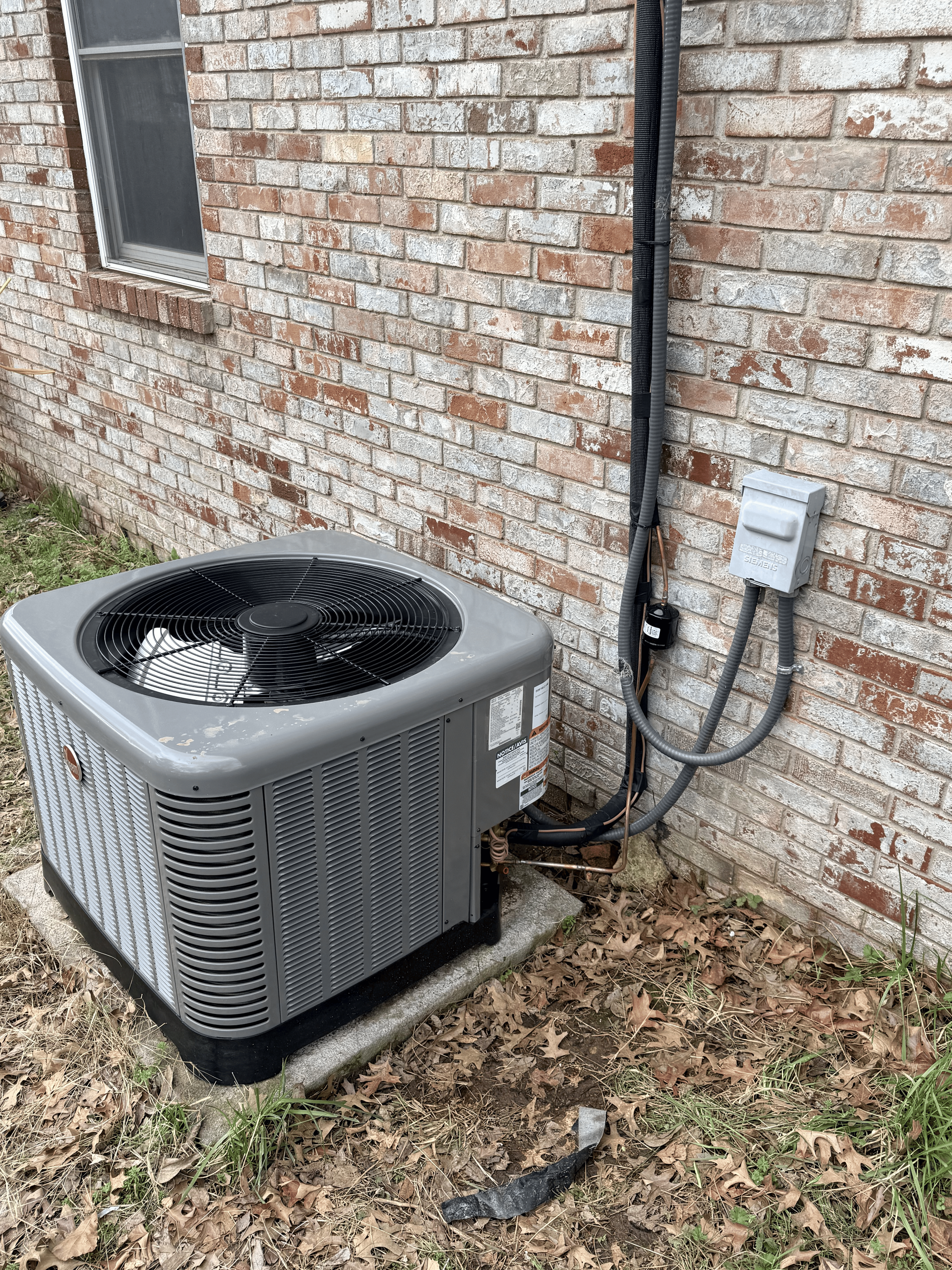 Outdoor air conditioner beside a brick wall.