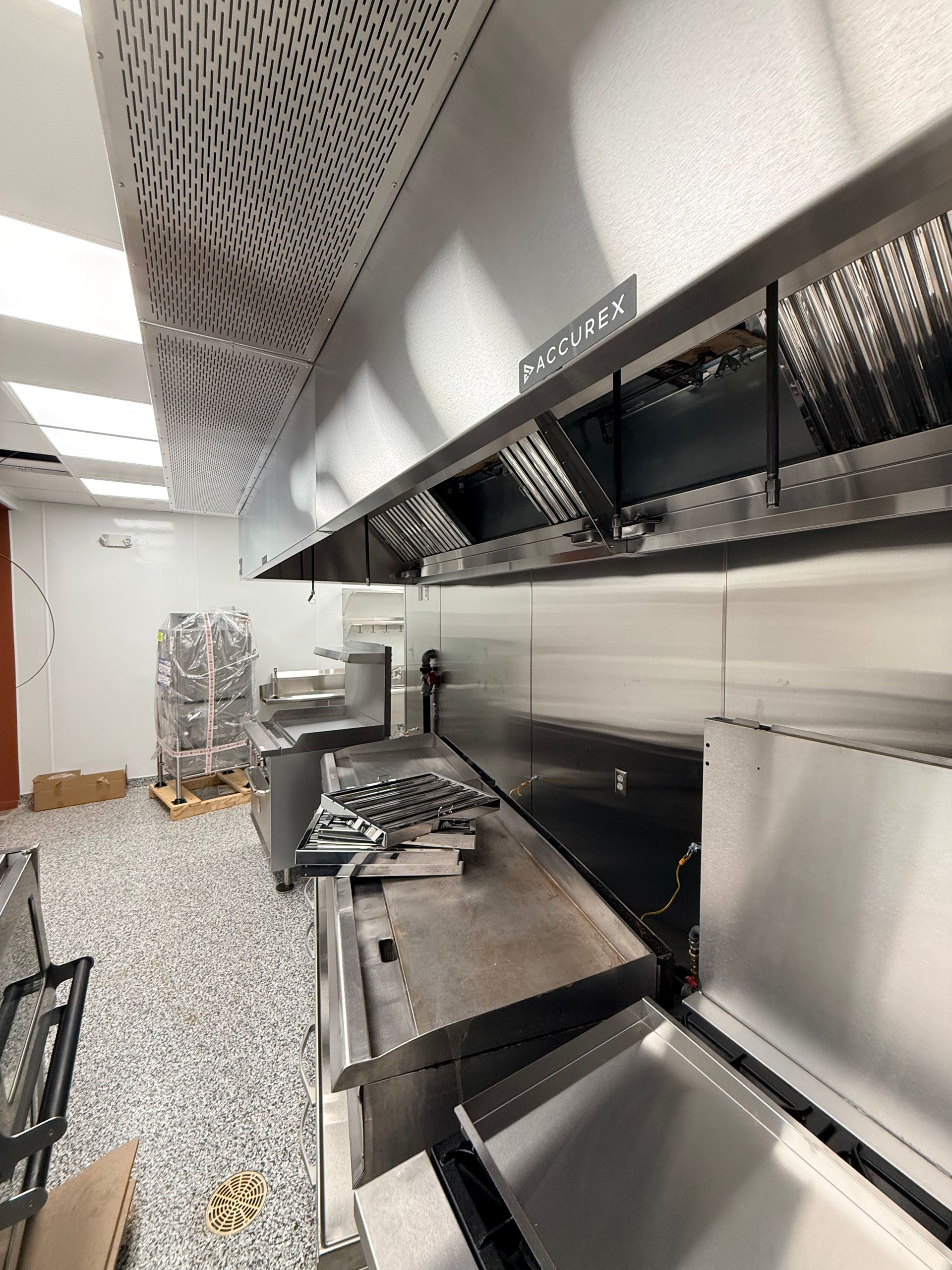 Modern stainless steel kitchen with grills, hood vents, and patterned metal ceiling panels