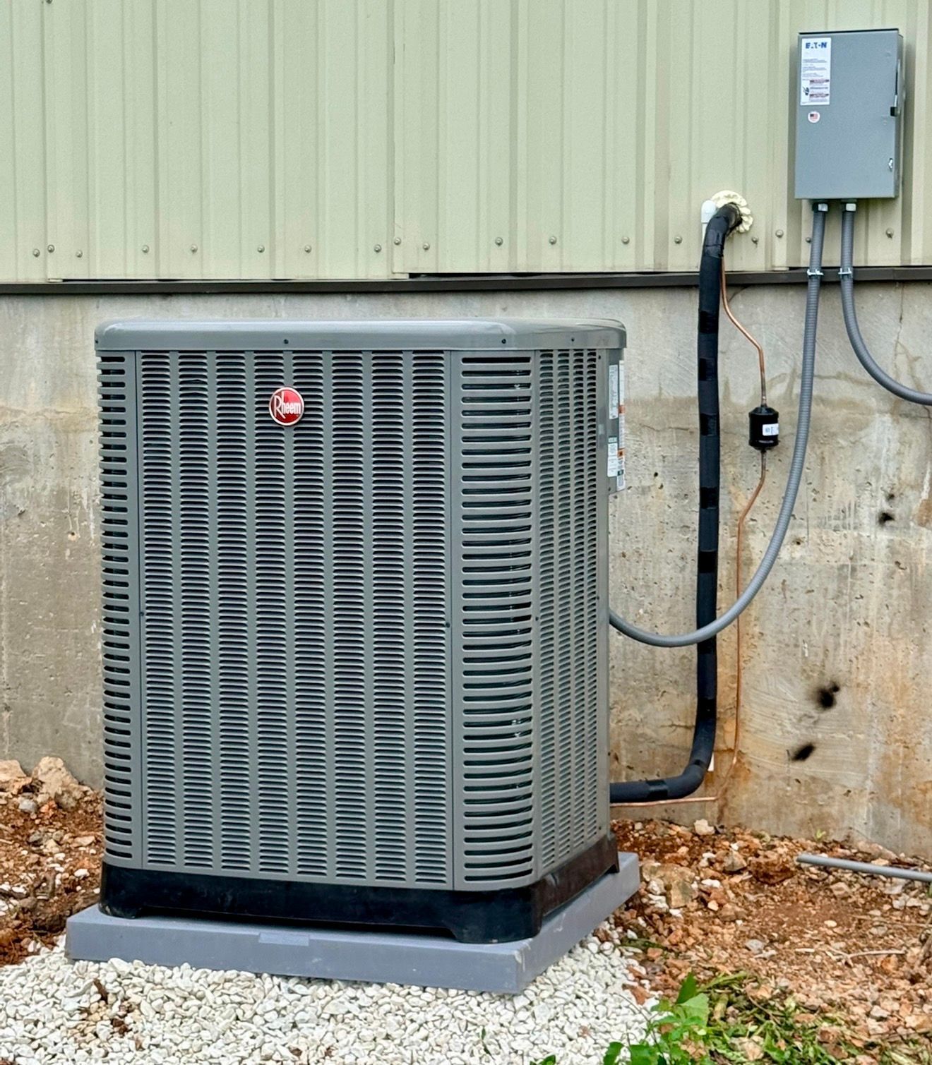 Outdoor HVAC unit beside a house wall with electrical box and conduit