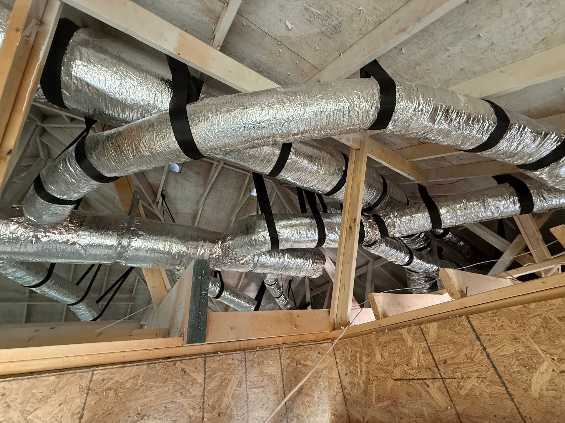 Exposed attic ductwork wrapped in silver insulation beneath wooden roof rafters