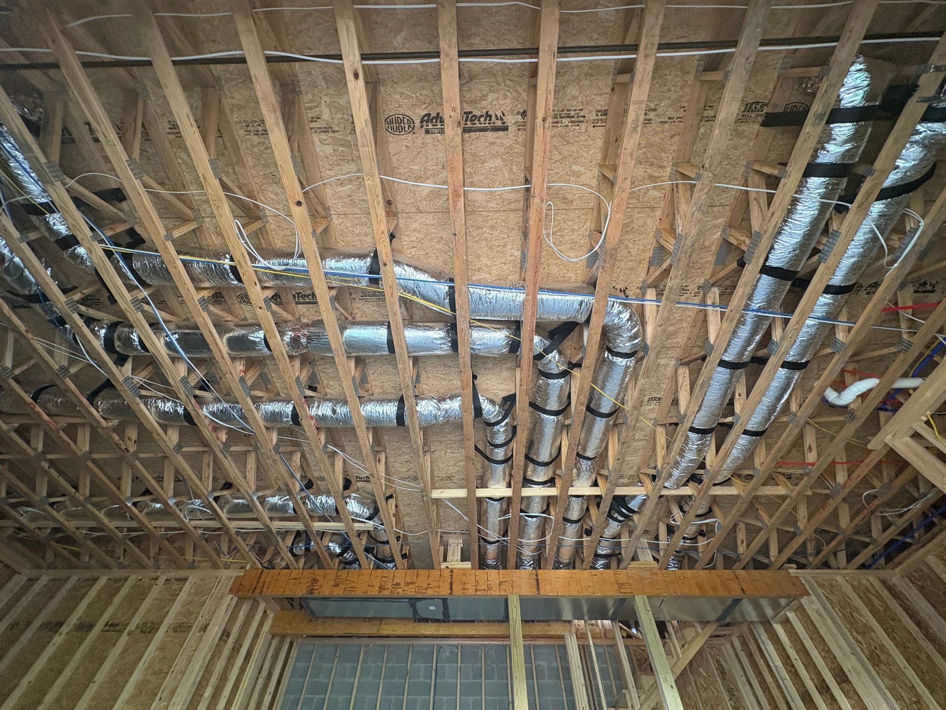 Exposed wooden ceiling framing with ducts and wires in an unfinished interior room