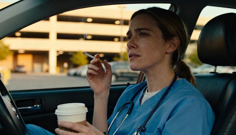 A tired but determined Columbus nurse sitting in her car after a long shift, holding coffee in one hand and a cigarette in the other conflicted about smoking
