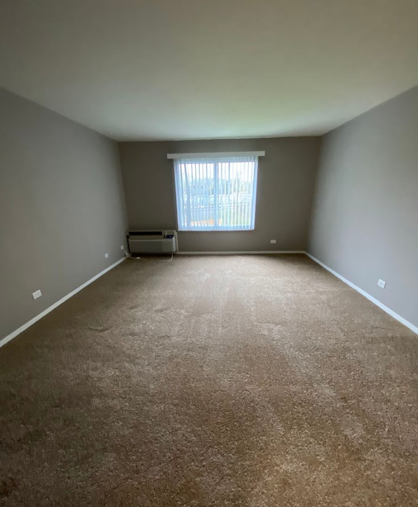 An empty living room with a large window and brown carpet.