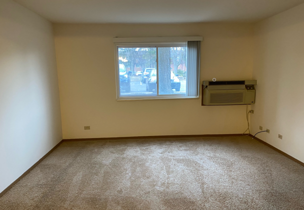 An empty living room with a window and air conditioner.