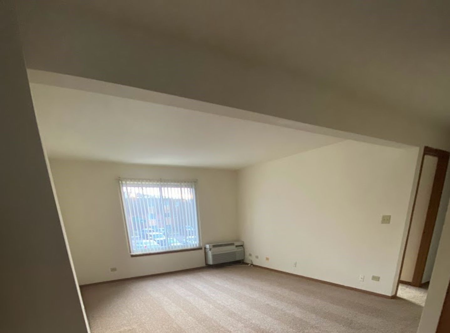 An empty living room with a window and a heater.