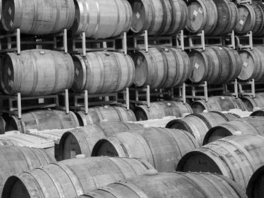 Rows of stacked wooden wine barrels stored in a dimly lit warehouse.