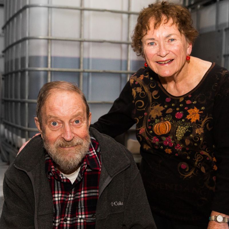 A smiling couple posing for a photo in front of a large, industrial metal storage tank.