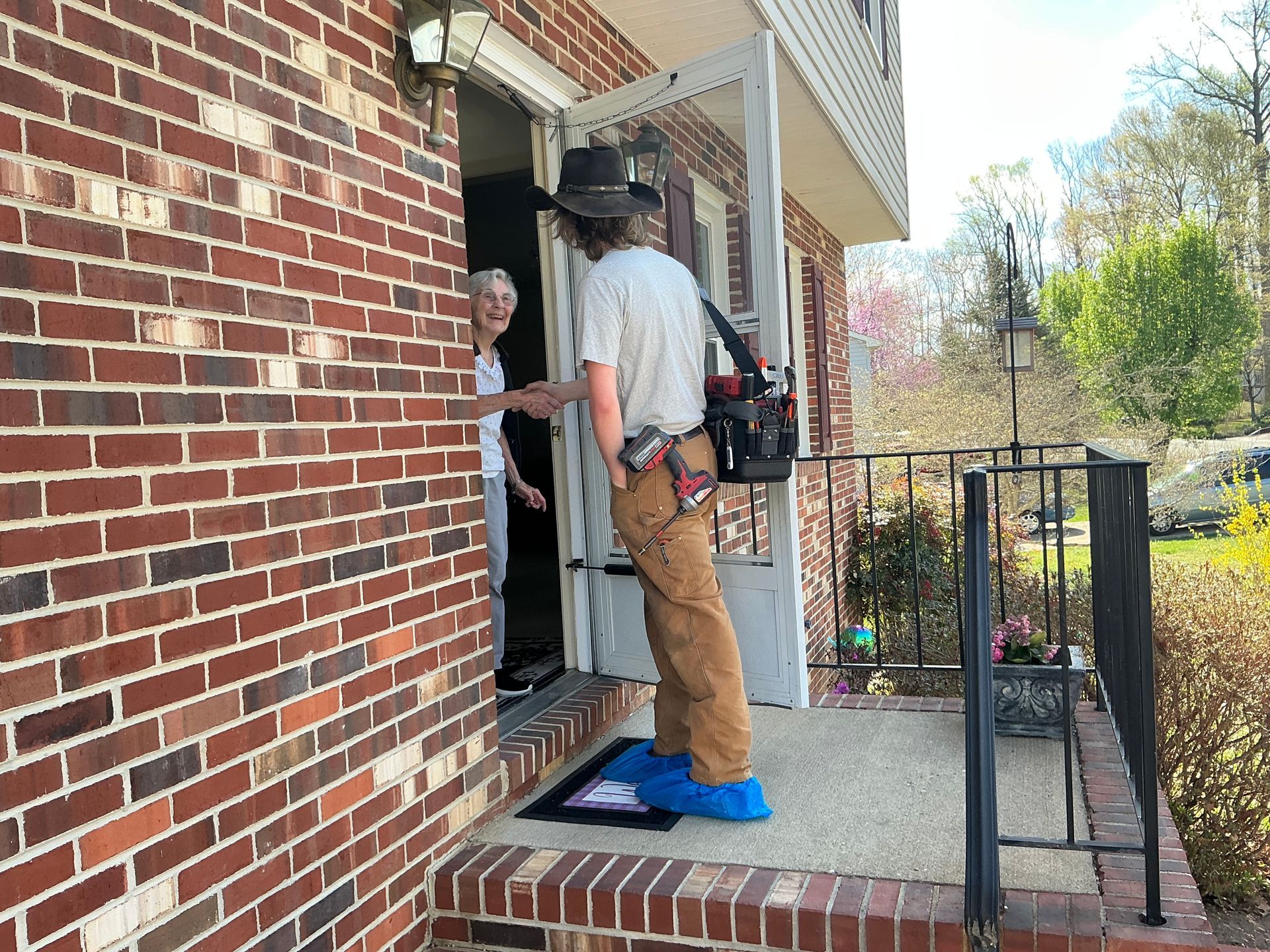 A man is standing on the porch of a brick house talking to a woman.