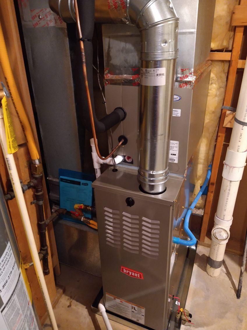 A furnace is sitting in a basement next to a water heater.