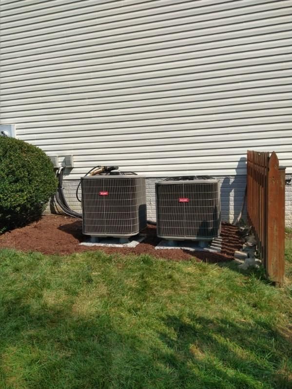 Two air conditioners are sitting on the side of a house.