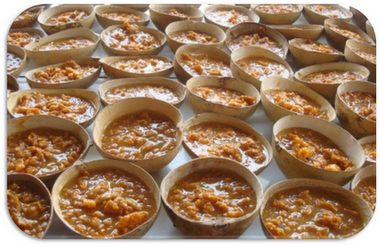 Filas de pequeños cuencos redondos de madera llenos de un alimento texturizado de color marrón.