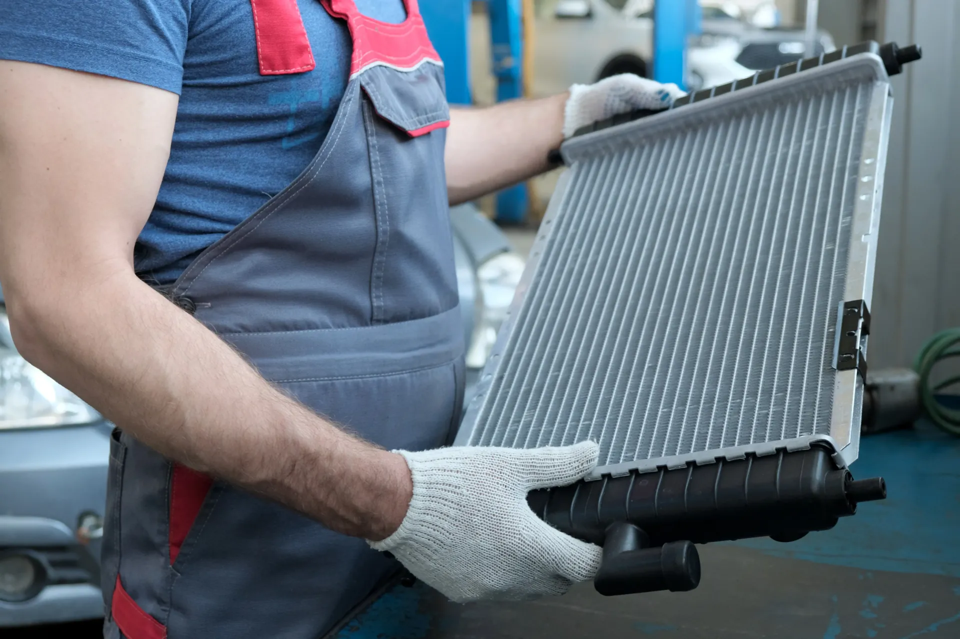 Trabajador con guantes sujetando un radiador de coche en un taller de reparación de automóviles.