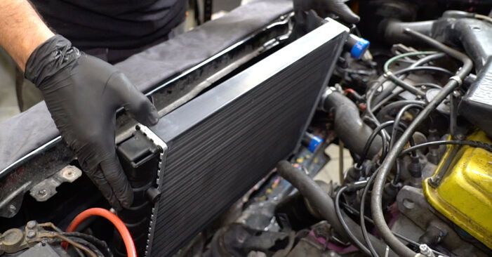 Mecánico sosteniendo un radiador negro junto a un compartimento del motor con mangueras y herramientas.