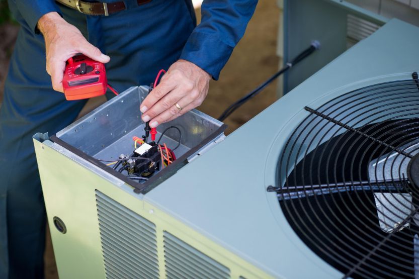 A man is working on an air conditioner with a multimeter.