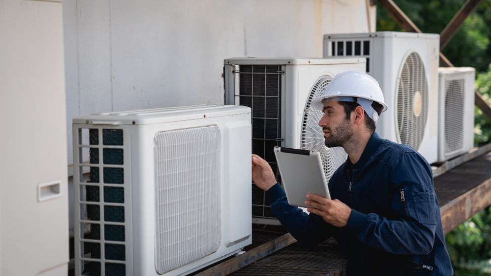 A man is looking at a tablet while standing next to a row of air conditioners.