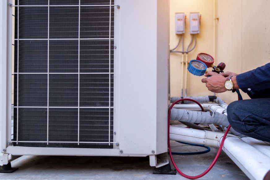 A man is working on an air conditioner outside of a building.