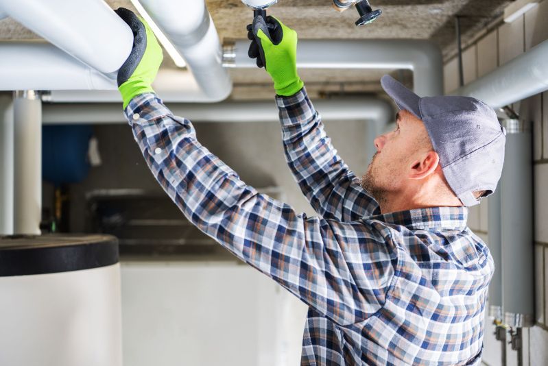 A man is working on pipes in a basement.