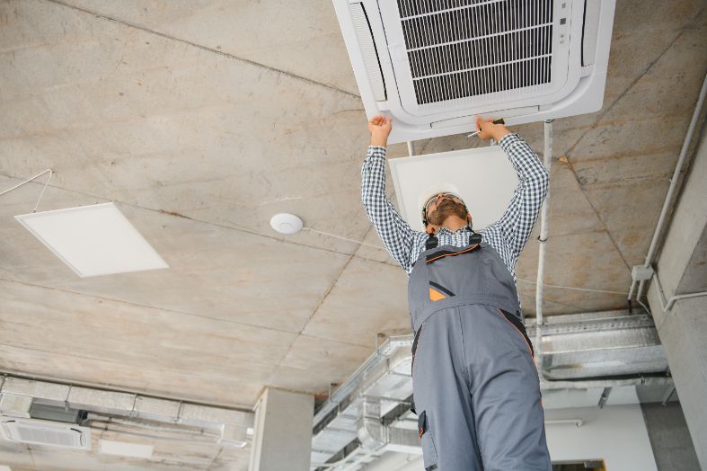 A man is hanging from the ceiling while installing an air conditioner.
