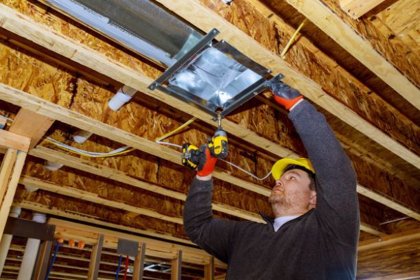 A man is working on a light fixture in the ceiling of a building.