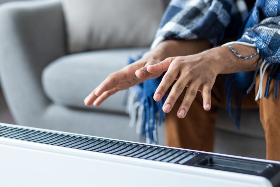 A person is sitting on a couch with their hands on a heater.