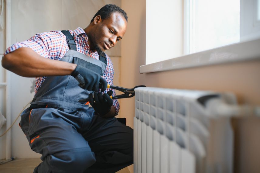 A man is kneeling down fixing a radiator in a room.