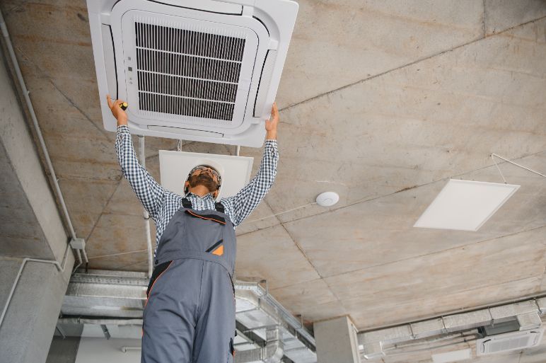 A man is installing an air conditioner on the ceiling of a building.