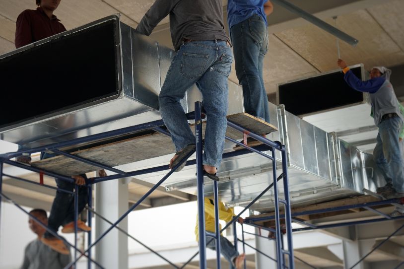 A group of men are working on a ventilation system on scaffolding.
