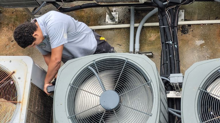 A man is working on an air conditioner on the roof of a building.