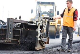 Male road worker standing by machines paving — Asphalt services in Denver, CO
