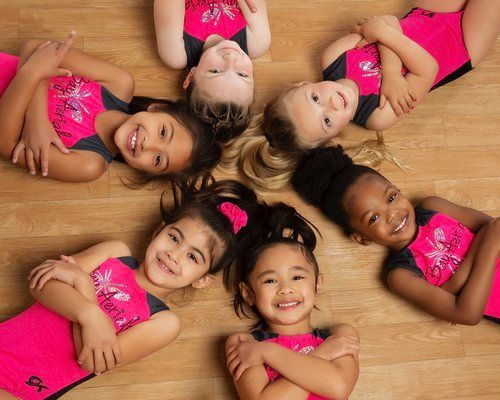 A group of young girls are laying on the floor in a circle.