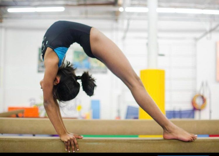 A female gymnast is doing a handstand on a balance beam.