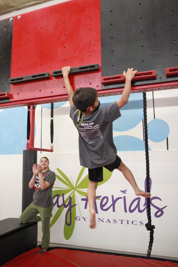 A boy is climbing a monkey bars in front of a sign that says bay aerials