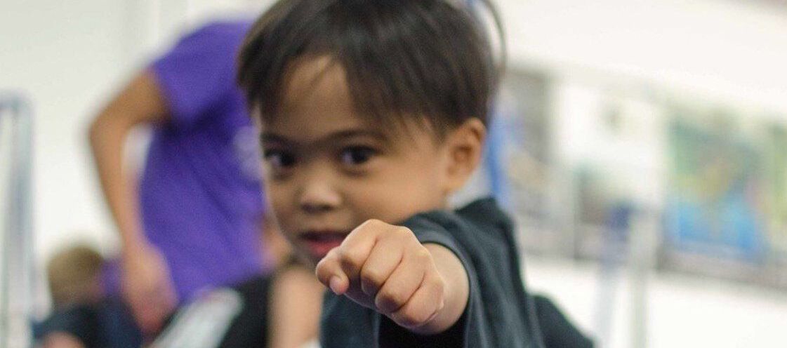 A young boy pointing at the camera with a blurry background
