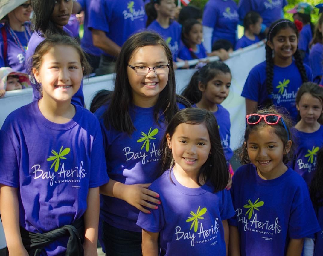 Children in blue shirts with logo, smiling outdoors.