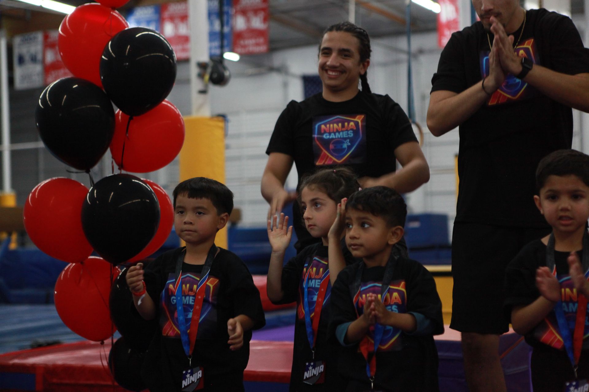 Children with balloons and medals standing with adults; indoors.