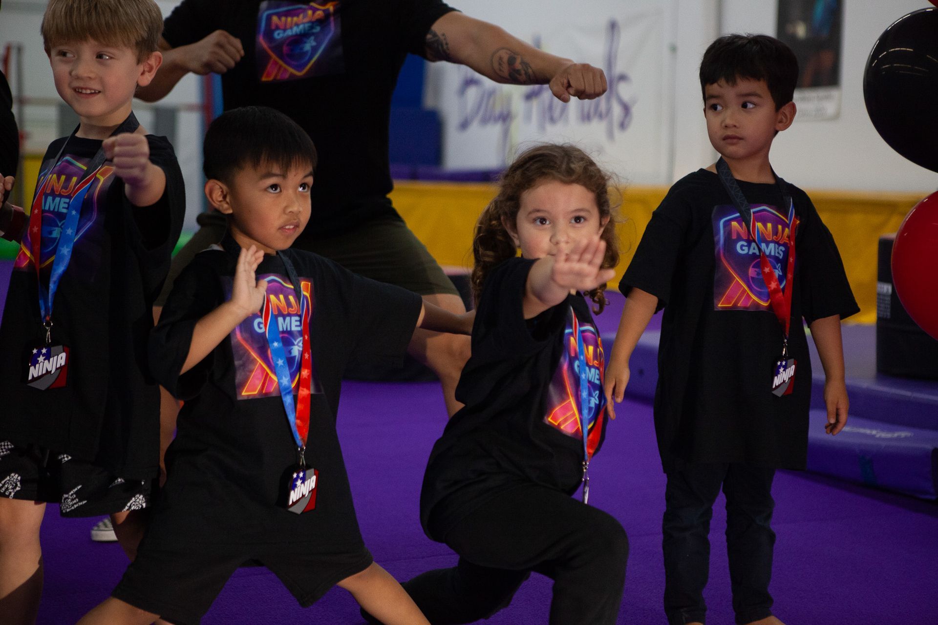 Children in black shirts practicing martial arts, purple mat background.