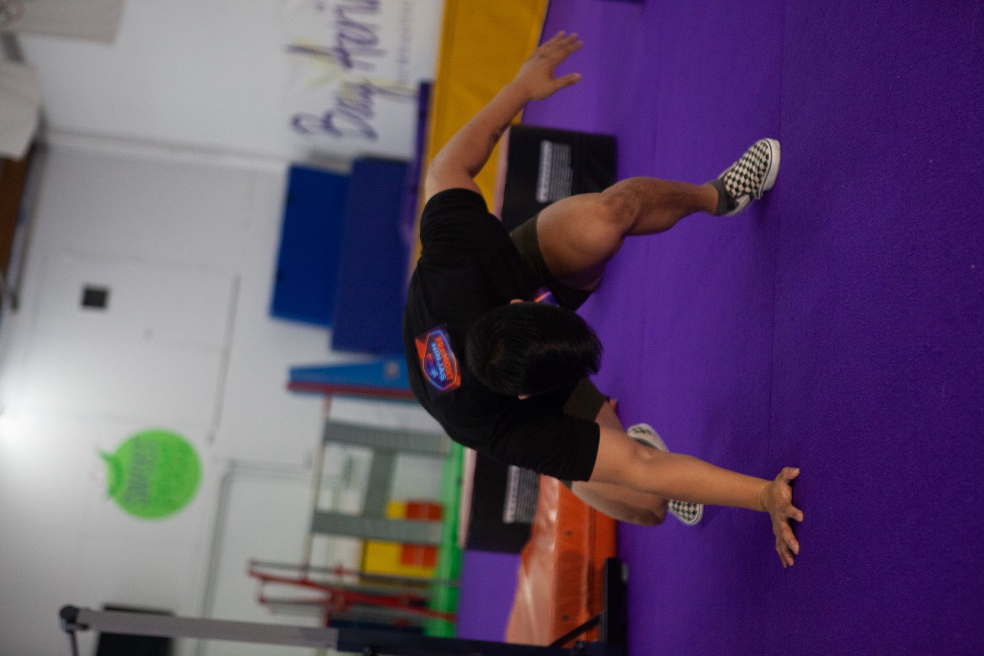 Gymnast in a handstand transition on a purple mat, arms extended, wearing black.