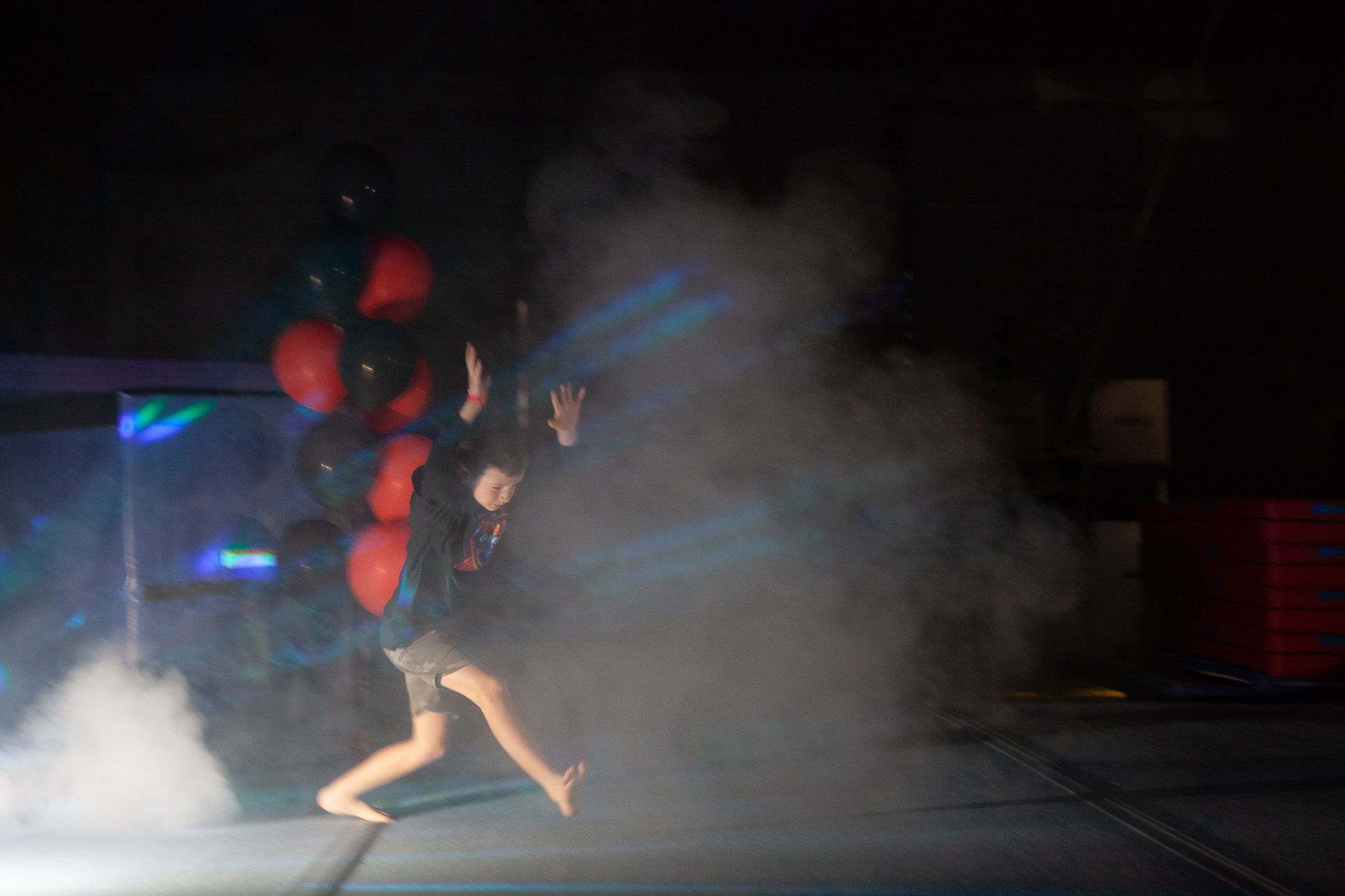 Person running with balloons through fog on a stage. Balloons are black and red.